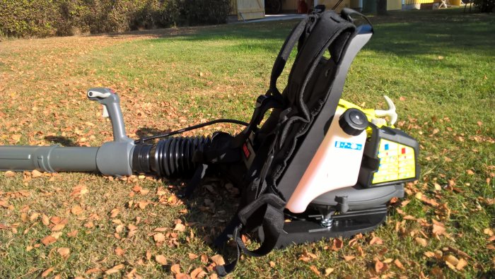 Ryobimaskin med förlängt blåsrör gjord av plastflaska, mot bakgrund av gräsmatta med löv.