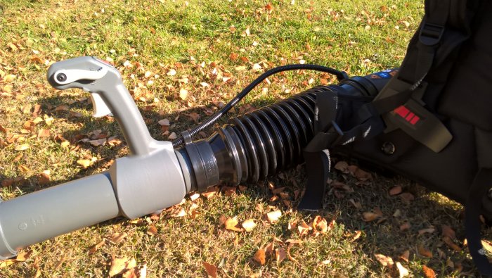 Ryobimaskin med förlängningsbit gjord av plastflaska på blåsröret, mot gräsmatta med löv.