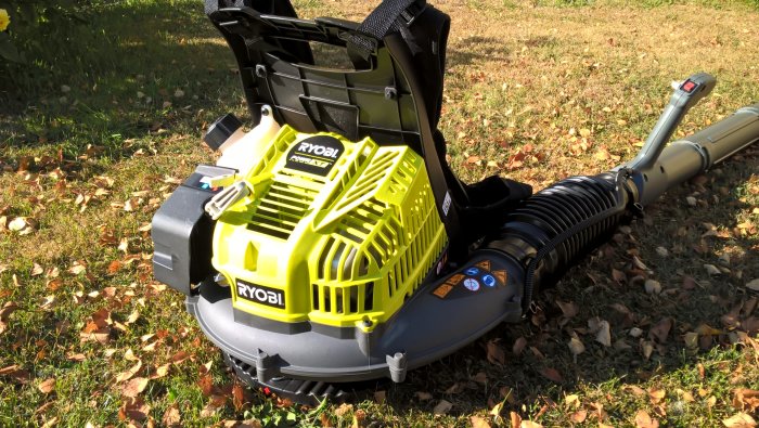 Ryobi lövblås med förlängt blåsrör av plastflaska och synlig komfortabel sele på gräsmatta med löv.