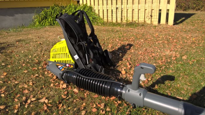 Ryobimaskin med förlängt blåsrör av plastflaska och stabil sele, mot gräs- och lövbeklädd mark.