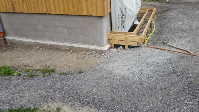 Ny gjuten toppkant på mur av leca och form för betongplatta till förråd vid byggnad under arbete.