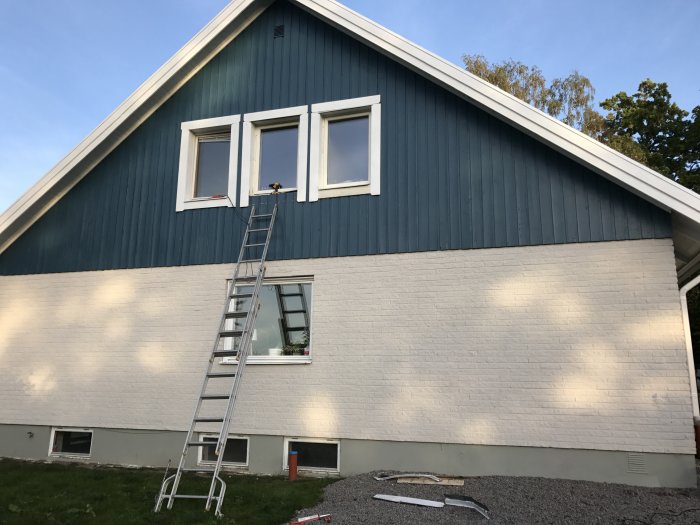 En stege lutad mot en husvägg med nyinstallerade fönster på övervåningen och isoleringsmaterial synligt.