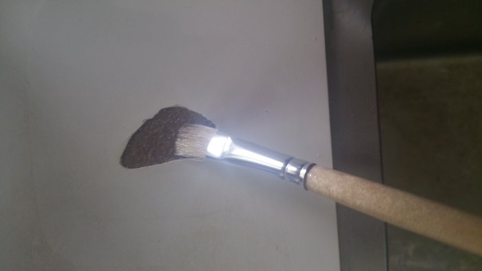 En borste applicerar trälack på en skada på en laminatbänkskiva för reparation.