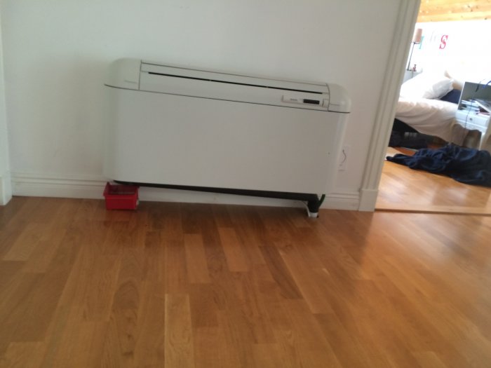 Luftkonditioneringsenhet med droppande vatten samlas i en röd behållare på parkettgolv.