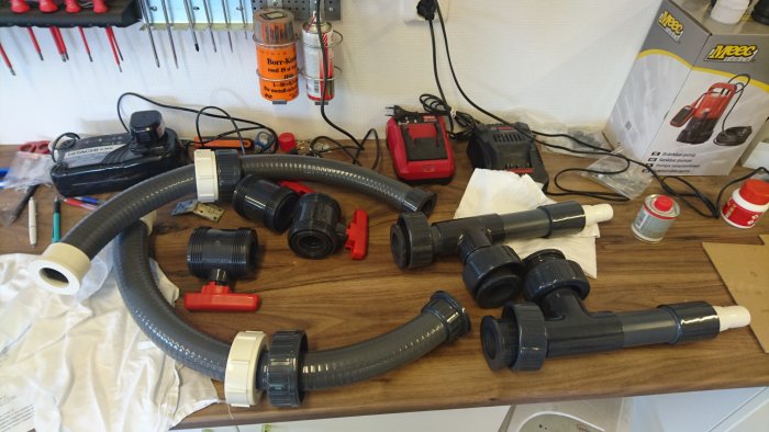 Delar till en bypass anordning: slangar och PVC-fittings på ett arbetsbord med verktyg och byggmaterial.