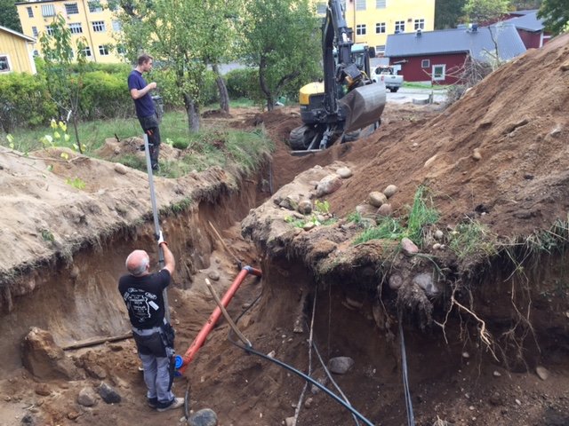 Två män arbetar vid en stor grävning med synliga avloppsrör vid en husgrund.
