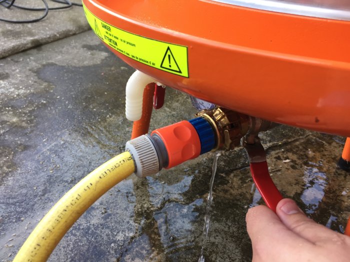 Någon öppnar en tappkran på en orange äppeljuicepress för att fylla en gul slang med nygjord must.