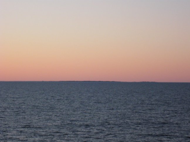 Sommarnattsutsikt över Kvarken med landmassan Gaddan i horisonten under en graderad himmel.