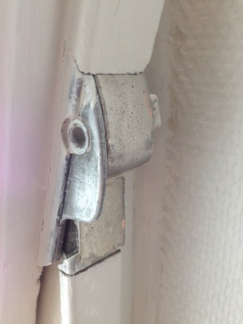 Närbild på ett öppet gammalt Fix-beslag för pivåfönster vid fönsterkarm, visande slitage och behov av justering.