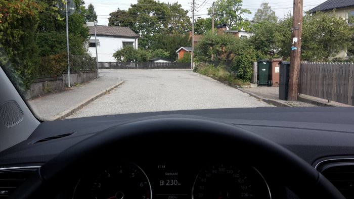 Bilens instrumentbräda och utsikt över en tom grusväg i ett stilla villaområde.