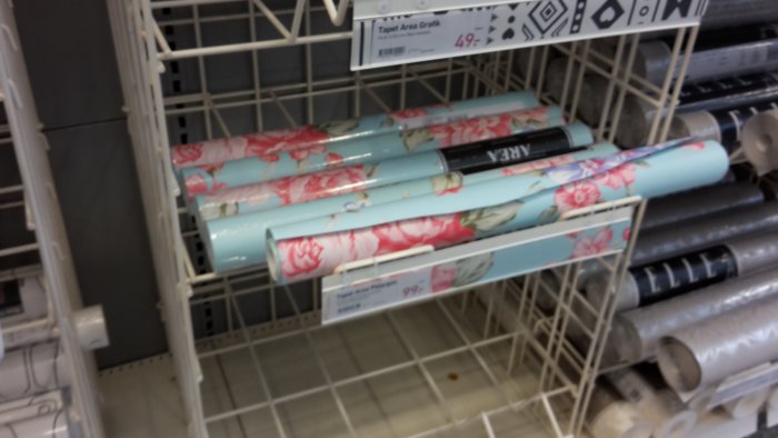 Rullar med blommigt tapet i affärshylla, prislappar synliga.