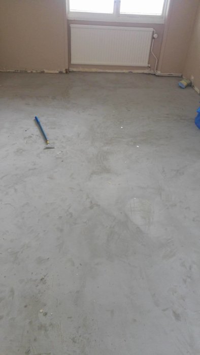 Upprivet golv med synliga fuktfläckar och ett tunt lager flytspackel över betongplatta i ett renoverat rum.