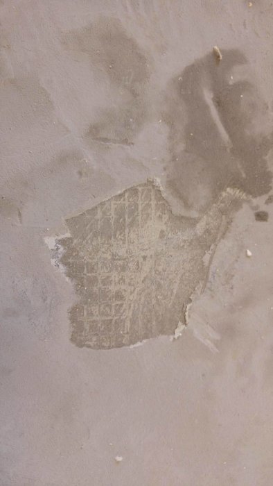 Fuktfläckar på flytspacklad betong med skrapade bitar av material som liknar papper.