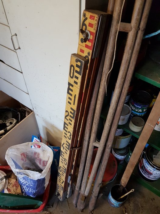 Gamla måttstockar och verktyg lutade mot en vägg i ett stökigt förråd.