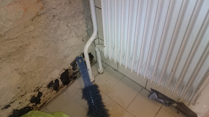 Element och rör vid skadad vägg med synlig mögel och spillror.