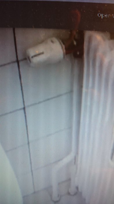 Suddig bild på en handdukstork monterad på vit kakelvägg bredvid en radiator.