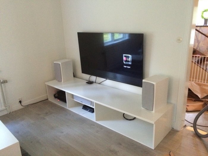 TV och högtalare på vit TV-bänk med osynlig kabeldragning och öppna fack, inomhusmiljö.