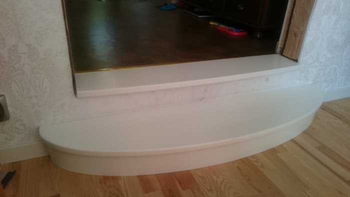 Nybyggd, vit, halvrund trapprototyp nära en vägg, med första steget i trä och övre i marmorlook, ersätter gammal trappa.