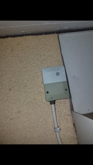 Grå eldoslåda med kabel monterad på en strukturerad vägg, nära ett hörn och golv.
