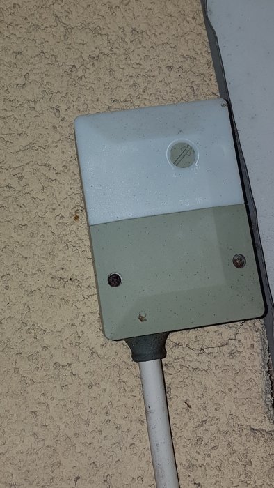 Elektrisk dosa på vägg utomhus med kabel som ansluter från nedre delen och misstänks för belysningsproblem.