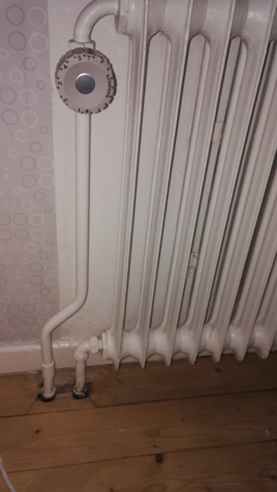 Vit radiator med termostatventil inställd mellan min och max i en inomhusmiljö.