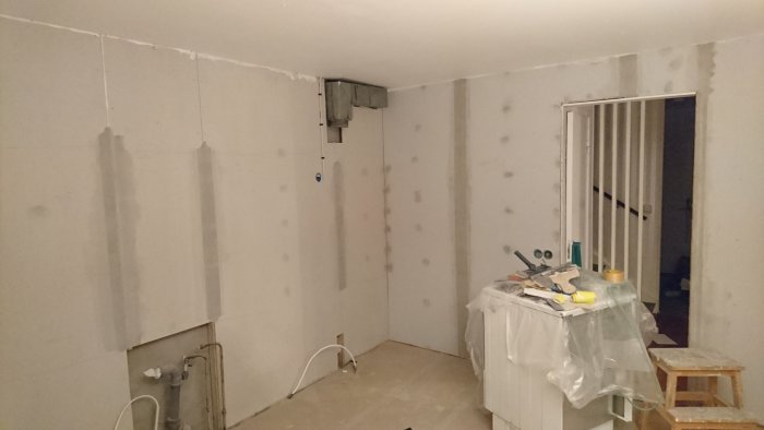 Ett under renovering kök med gipsskivor på väggarna och skyddsplast över köksö.