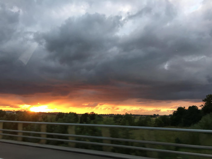 Solnedgång med dramatiska moln sedd genom bilruta, upptagning från en svensk landsväg.