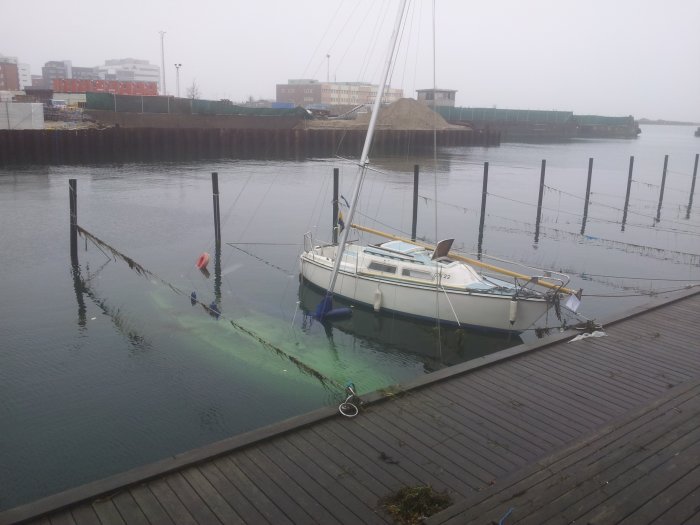Segelbåt sjunken vid kaj med synlig köl i disigt väder.