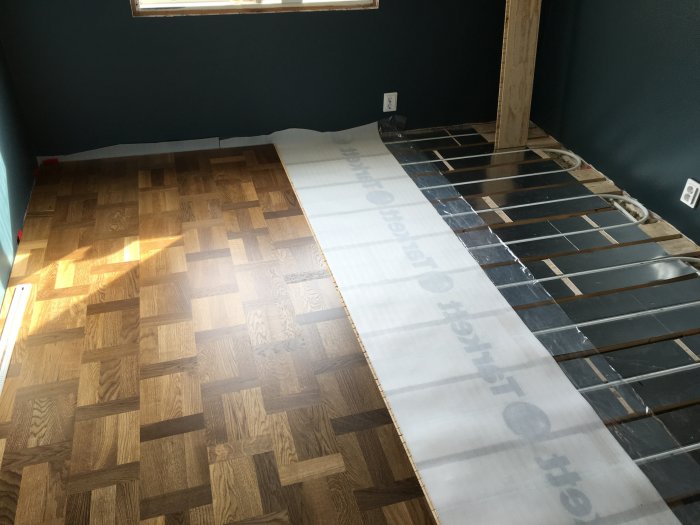 Installationsprocess av trägolv där en del av golvet är färdigt och resten har synliga glespaneler och en rulle golvunderlägg.