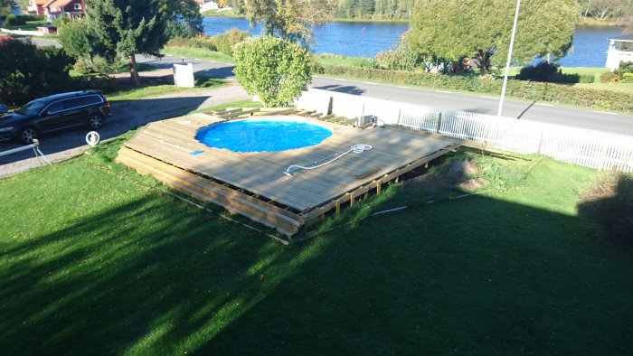 Rund pool med blått soltäcke omgiven av nybyggd trädäck vid ett bostadshus.