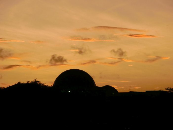 Silhuett av byggnader mot en himmel med solnedgång i orange och gula toner.