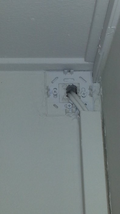 Ett öppet väggfäste med synliga snäppfästen och fiberkabel, i väntan på ett passande lock.