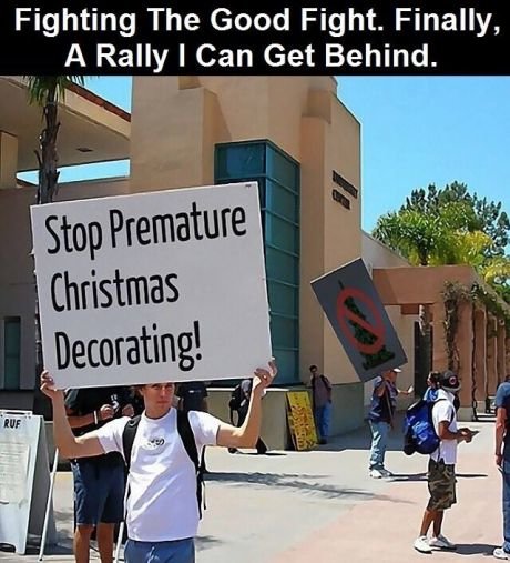 Person håller en skylt med texten "Stop Premature Christmas Decorating!" vid en offentlig demonstration.