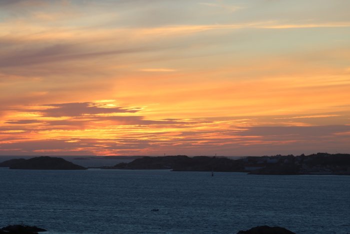 Solnedgång över havet vid västkusten med orange himmel och silhuett av öar.