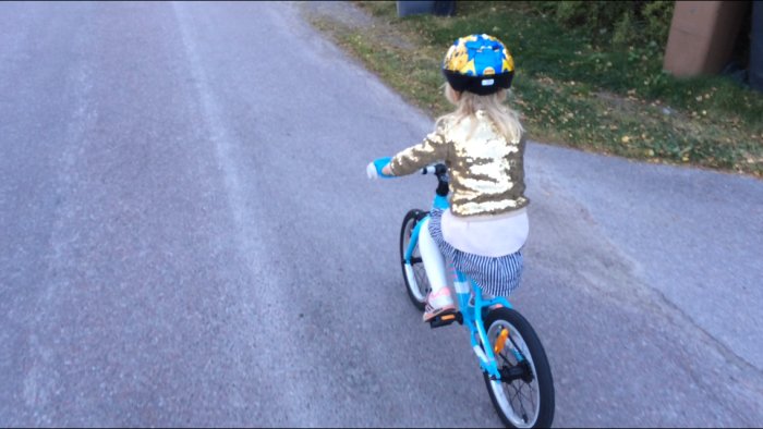 Barn i guldfärgad paljettröja cyklar på blå och vit cykel utomhus.