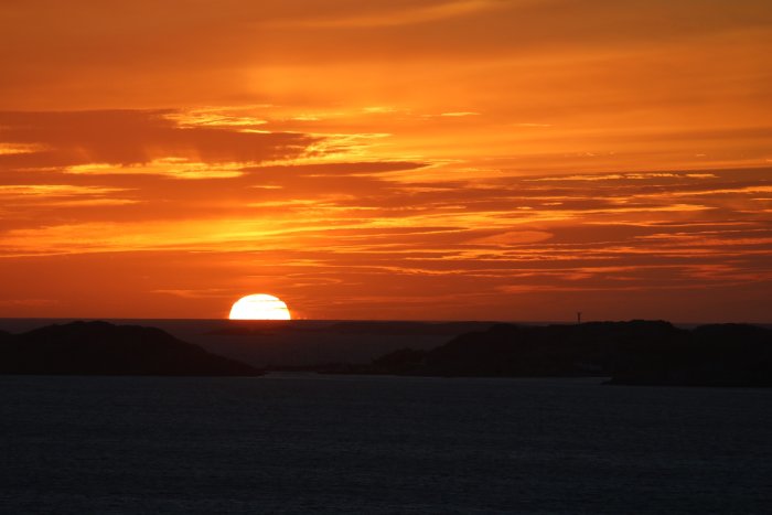Solnedgång med orange himmel över hav och silhuett av kustlinje.