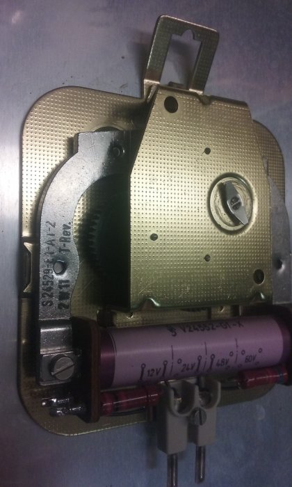 Gammalt urverk med märkning 50Hz/1,10W och flera kondensatorer, inklusive en med voltmärkningar från 12V till 60V.