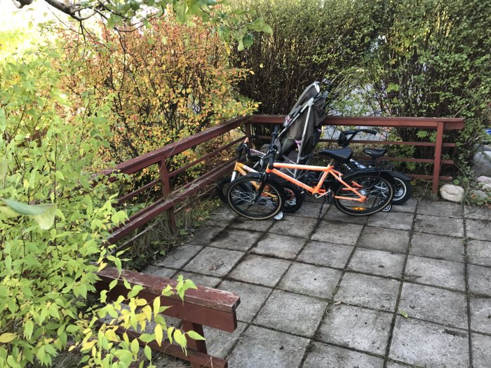 Ett oövertäckt cykelställ i en trädgård med flera cyklar och omgiven av grönska och en träbänk.