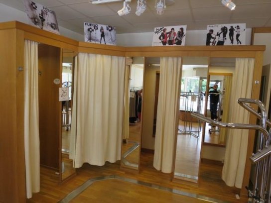 Återbrukad butiksinredning omgjord till klädkammare med gardiner och inbyggda hyllor, speglar på väggen.