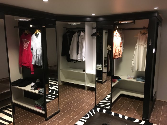 Renoverad klädkammare med svartmålade, inbyggda garderober och hyllor, fyllda med kläder och belysta ovanifrån.