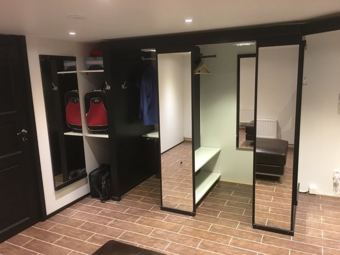 Nybyggd klädkammare med svart inredning, vita hyllor, klädhängare och en stor spegel, inomhusbelysning.