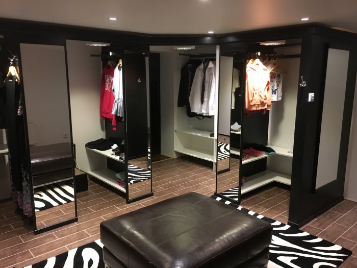 Nymålad klädkammare med inbyggda hyllor, öppna garderober och en sittpuff på ett zebra-mönstrat matta.