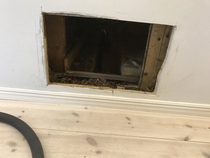 Öppning under trappa med gammal mineralull och träspill, bredvid en dammsugarslang.