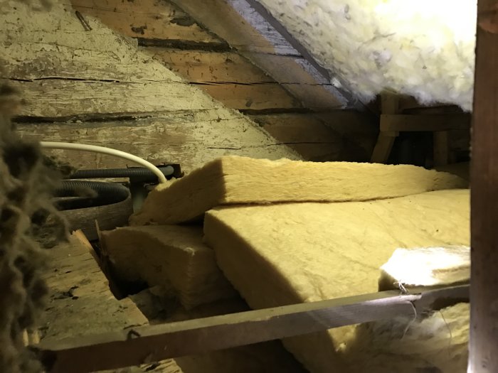 Utrymme under trappa med gammal mineralull och träplankor.