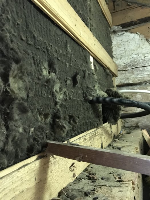 Gammal mineralull som tas bort under trappa, synliga träreglar och damm.