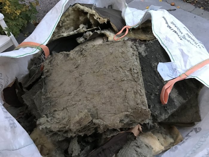 Gamla bitar av mineralull i olika färger samlade i en byggsäck utomhus.