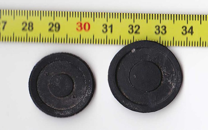 Två svarta runda föremål vid en måttstock som visar storlek i centimeter.
