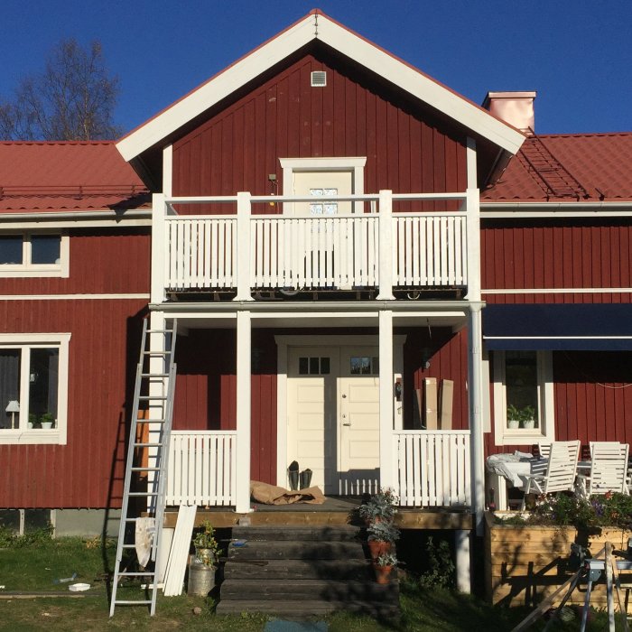 Ny målad farstukvist på ett rött hus med en stege lutad mot balkongen och färgburkar på marken.