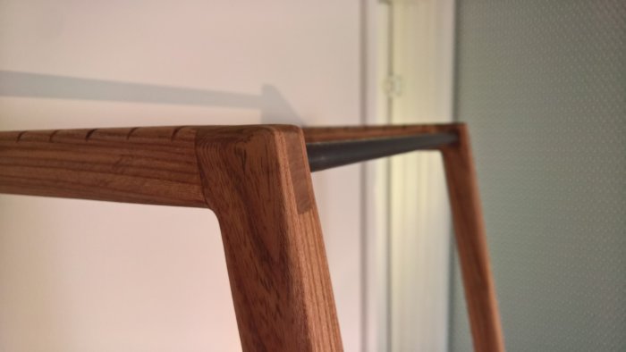 Klädhängare av alm och mörk järnstång, finish med Danish oil och "Black Walnut"-bets, hjärtformad detalj syns.