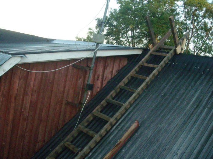 Hemmagjorda trästegar över hustakets nock för byte av gavelpanel, med säkring mot panelen.